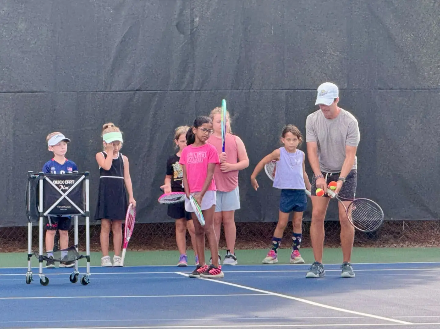 A coach feeding orange balls to a line of young juniors at Crooked Creek