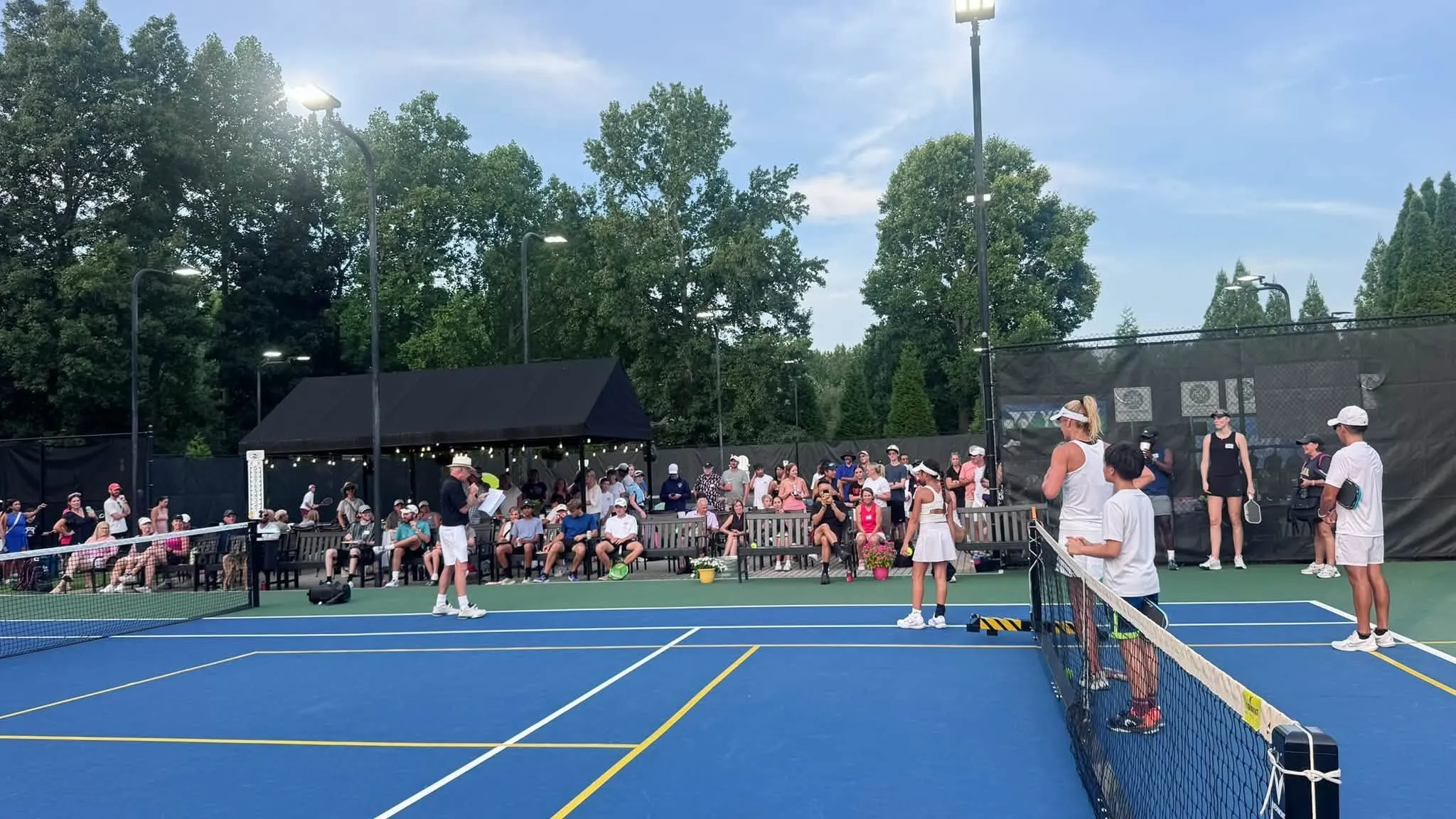 Players at the net on a lit court at Crooked Creek at dusk